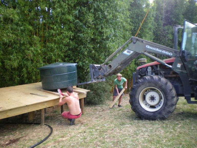 two boys working on a platform for a dark green vat being placed by forklift