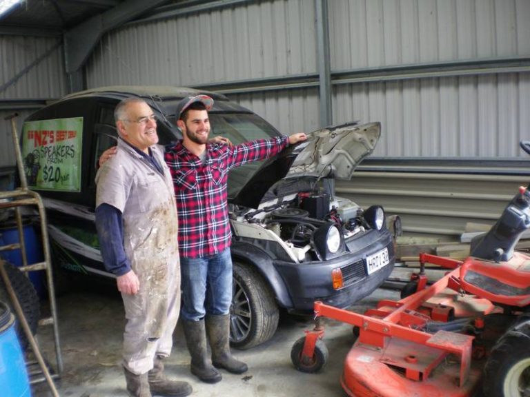 older man and younger man smiling while working on a car engine