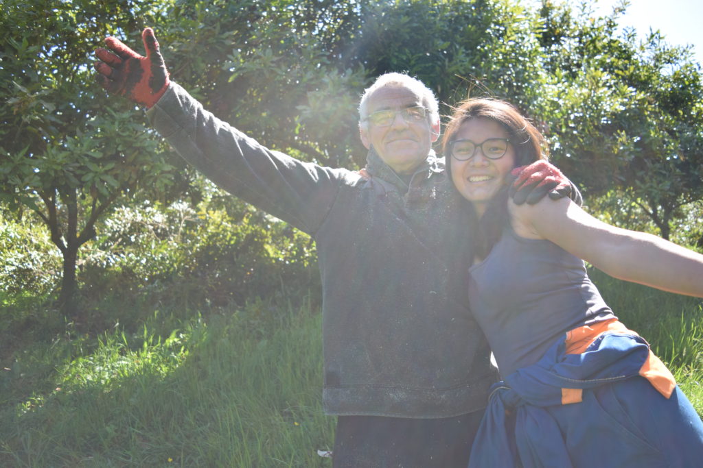 John and Isabelle smiling and standing in orchard, arms outstretched